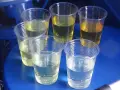 Sześć przezroczystych kubków z płynami o różnym zabarwieniu, od jasnego do ciemnożółtego. Prawdopodobnie próbki oleju napędowego do analizy.