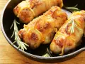 Involtini di pollo dorati e succulenti, legati con spago da cucina e guarniti con rametti di rosmarino, in una padella di ghisa.
