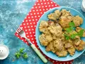 Piatto di fegatini di pollo impanati e fritti, guarniti con prezzemolo. Accanto, una forchetta e un sale e pepe.