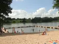 Słoneczne plaże na Mazurach tętnią życiem. Ludzie odpoczywają na piasku, kąpią się w jeziorze i spacerują po pomoście.