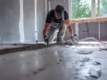 Budowlaniec wylewa betonową wylewkę, wyrównując ją ręcznie.