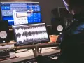 Tworzenie muzyki w domowym studiu. Na ekranach widać programy do edycji dźwięku, a w rękach gitarzysty gryf gitary.