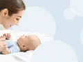 Uśmiechnięta mama pochyla się nad dzieckiem, które świadomie mówi "mama".