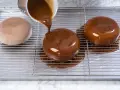 Dolce lucido ricoperto da una colata di cioccolato. La glassa scende sui lati, creando un effetto invitante.