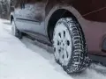 Un'auto marrone avanza su una strada innevata, le ruote dotate di pneumatici chiodati per affrontare il ghiaccio e la neve.