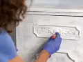 Mano enguantada aplica pintura a muebles pintados a la tiza en dos colores, dando un acabado desgastado y elegante.