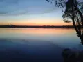 Zachód słońca nad jeziorem, z sylwetką elektrowni w oddali. Na wodzie pływają kaczki, a drzewo rzuca cień. Pogoria 3 w pięknych barwach.