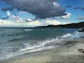 Onda che lambisce la spiaggia sabbiosa dell'Isola d'Elba, con il mare azzurro e nuvole scure nel cielo.