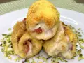 Tre involtini di pollo dorati e ripieni di formaggio filante e prosciutto, adagiati su un letto di pistacchi tritati.