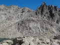 Vetta frastagliata di un monte rotondo, con rocce grigie e un lago alpino sullo sfondo.