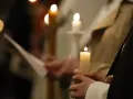 Dłonie trzymają płonące świece, symbolizujące poświęcenie ognia podczas uroczystości.