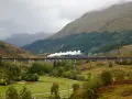 Parowóz z białym dymem mknie po kamiennym wiadukcie w szkockich highlands.