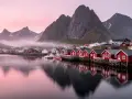 Röda fiskestugor vid vattnet i Lofoten, med berg och rosa himmel. En dröm om norrsken.