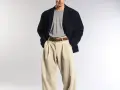 Uomo con spezzato giacca blu scuro, maglietta grigia e pantaloni beige a vita alta.