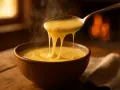 Une cuillère de crème de reblochon fumante s'étire au-dessus d'un bol, devant un feu de cheminée chaleureux.