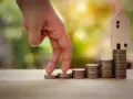Main qui monte les marches de pièces, symbolisant la croissance et la gestion des revenus fonciers. Une maison en bois au sommet.