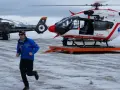 Ratownik w niebieskiej kurtce biegnie na tle dwóch helikopterów w Austrii, gotowych do akcji po lawinie.