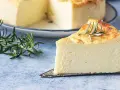 Una fetta di torta di ricotta soffice e dorata, guarnita con rosmarino, su un piatto da torta.
