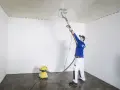 Pracownik szlifuje sufit, by go wyrównać. Odkurzacz zbiera pył.