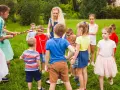 Des animateurs et des enfants jouent dehors dans l'herbe avec des cerceaux colorés.