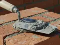 Kielnia z zaprawą na cegłach. Różne rodzaje kielni pomagają w precyzyjnym murowaniu.