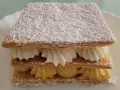 Delicioso milhojas de crema, con capas crujientes de hojaldre y rellenos de crema pastelera y nata montada, espolvoreado con azúcar glas.