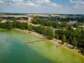 Letnie popołudnie nad jeziorem wielewskim. Tłumy plażowiczów, kąpielisko z pomostem i urokliwa miejscowość w tle.