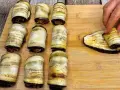 Nove involtini di melanzane pronti, uno viene arrotolato su una fetta di melanzana grigliata.