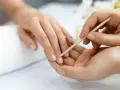 Delikatne dłonie poddawane zabiegowi manicure biologiczny. Skórki są starannie odsuwane patyczkiem, przygotowując paznokcie do dalszej pielęgnacji.
