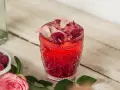 Orzeźwiający drink z malinami, ozdobiony płatkami róż i świeżymi malinami. Idealny na letnie popołudnie.