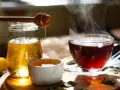 Une cuillère en bois verse du miel doré dans une tasse de thé fumante. Un délice réconfortant de miel dans eau chaude.
