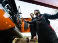 Dwóch mechaników w kombinezonach przeprowadza konserwację maszyn budowlanych. Jeden z nich wskazuje na silnik.