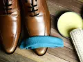 Brązowe buty, niebieska ściereczka, pędzel i wosk. Dowiedz się, jak impregnować buty domowym sposobem, by służyły latami.