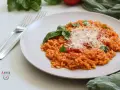 Un cremoso risotto al pomodoro, guarnito con basilico fresco e parmigiano grattugiato, pronto per essere gustato.
