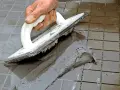 Handen använder en spackel för att foga om kakel.