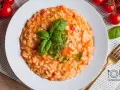 Pyszne risotto z pomidorami, udekorowane bazylią i pesto, czeka na talerzu. Obok świeże pomidorki i złoty widelec.