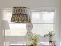 Un abat-jour suspendu avec un motif floral bleu et des volants, une excellente idée déco abat jour. Des assiettes décoratives et des fleurs complètent la scène.