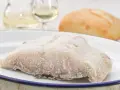 Un trozo de pescado en blanco, escarchado, listo para cocinar. Acompañado de pan y vino blanco.