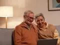 Uśmiechnięta para seniorów przegląda coś na laptopie. Zastanawiają się, czy zwolnienia lekarskie mają wpływ na wysokość emerytury.