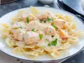 Pyszny makaron farfalle z kawałkami łososia w kremowym sosie, posypany natką pietruszki. Idealny na szybki obiad.