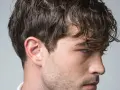 Perfil de hombre con cabello castaño ondulado y barba incipiente. Su corte de pelo es un rapado al 3 en los laterales.
