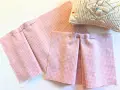 Tissu rose à carreaux avec des plis épinglés, montrant comment faire des plis en couture avec une fourchette. Coussin à épingles en arrière-plan.