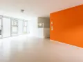 Jasne, nowoczesne wnętrze z pomarańczową ścianą i podłogą z **mikrobetonu**. Duże okna wpuszczają dużo światła.