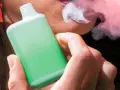 Persona vapeando un dispositivo verde, exhalando vapor. Una imagen que ilustra la diferencia entre vapear y fumar.