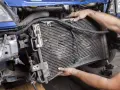 Mechanic removing a car's AC condenser, which blows hot air, for repair.