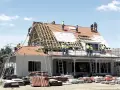 Ekipa budowlana w kaskach remontuje dach domu, używając drabin i rusztowań.