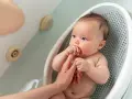 Niemowlę w wanience, rodzic sprawdza, ile stopni powinna mieć woda do kąpieli niemowlaka, by była idealna.