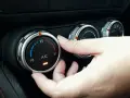Dłoń reguluje pokrętłem temperaturę klimatyzacji w samochodzie, ustawiając ją na 25 stopni.