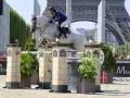 Un cavalier et son cheval blanc, Rahotep de Toscane, franchissent un obstacle à Paris, avec la Tour Eiffel en arrière-plan.