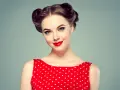 Eleganckie fryzury retro na wesele, z kręconymi kokami i czerwoną sukienką w grochy.